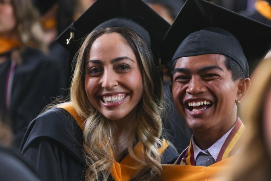 Two students smile in cap and gown at graduation